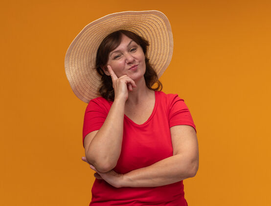 中年身穿红色t恤 头戴夏帽 满脸笑容的中年妇女站在橙色的墙上女人帽子年龄