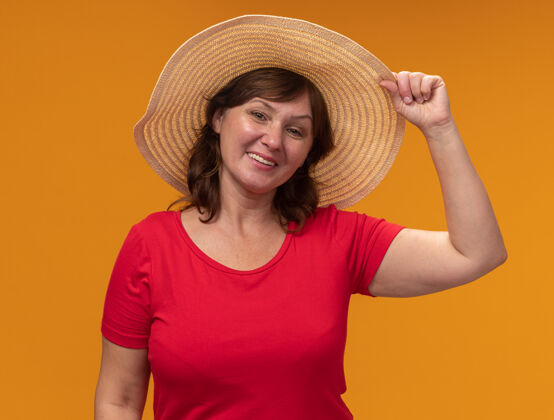 帽子身穿红色t恤 头戴夏帽的中年妇女站在橙色的墙上 快乐而积极地微笑着欢呼女人立场