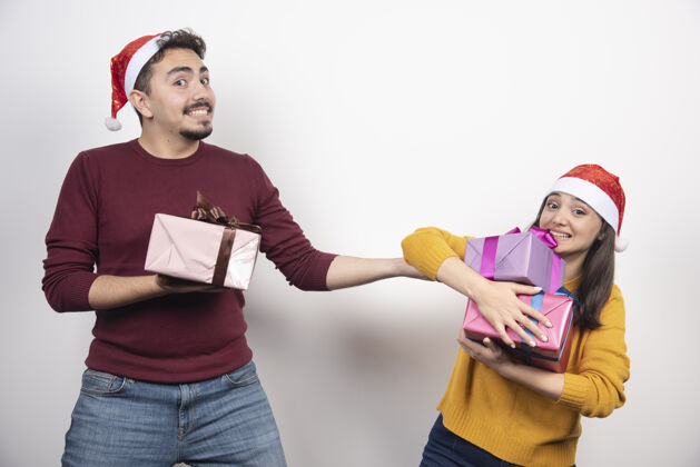 圣诞帽在白色的墙上挂着圣诞礼物的幸福夫妇摆姿势人类模特
