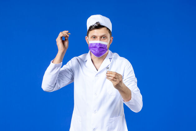 大流行前视图中的男医生穿着医疗服和口罩持有疫苗和注射在蓝色疫苗男医生药