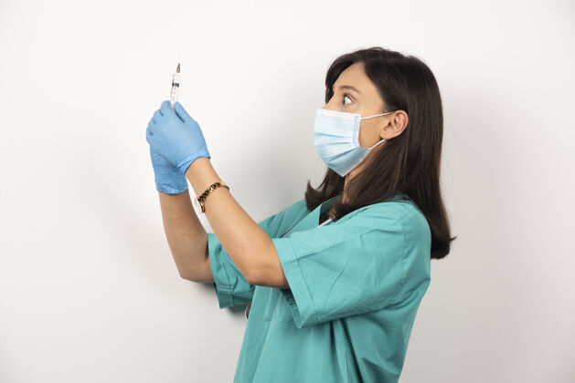听诊器年轻的医生戴着医用面罩和手套 拿着白色背景的注射器注射器职业疫苗