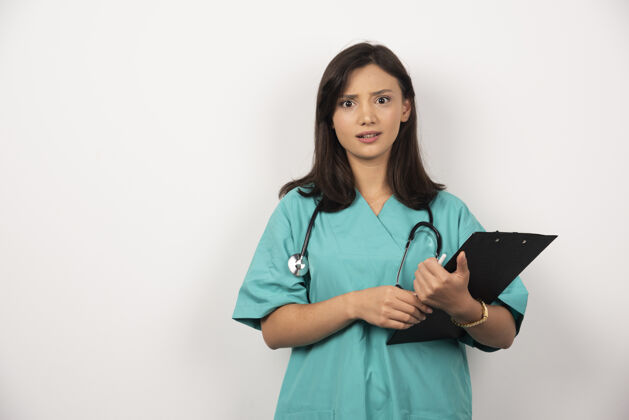 妇女带听诊器和剪贴板的医生在白色背景上看起来很惊讶工人工作保健