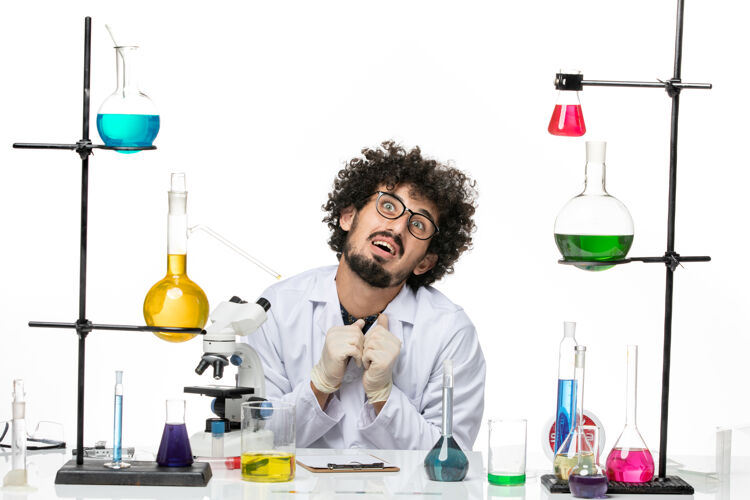溶液正面图身着医疗服的男性化学家正坐在桌子前面 浅白的空间里放着溶液实验室外套专业实验室