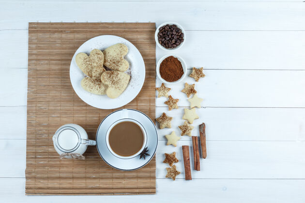 糖一壶牛奶 一杯咖啡 放在铺有咖啡豆和面粉的垫子上的心形饼干 星形饼干 白色木板背景上的肉桂色顶视图甜点餐垫庆典