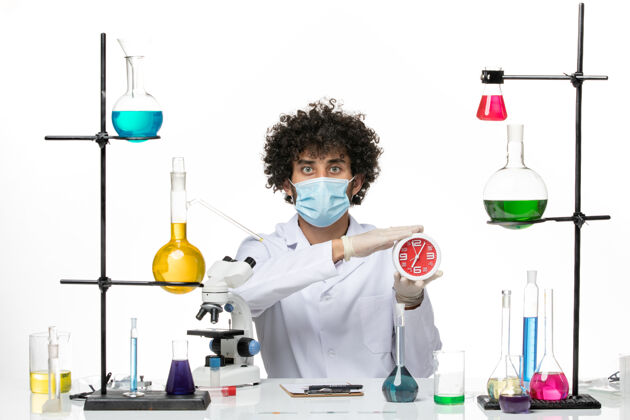 医学正面图：男药剂师 穿着医疗服 戴着面具 在白色的空间里拿着红色的时钟科学男性男性化学家