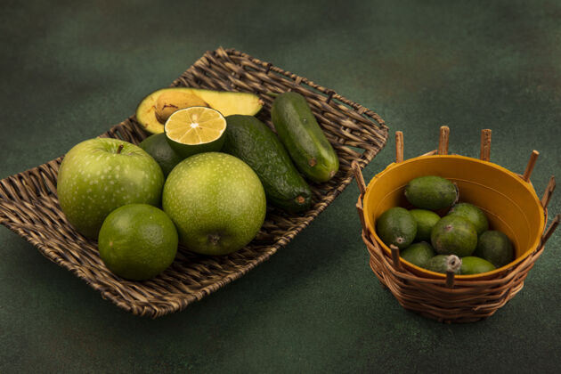 鳄梨顶视图的柳条托盘的健康食品 如绿色的苹果 酸橙 鳄梨和黄瓜与feijoas桶上的绿色表面黄瓜食物午餐