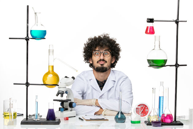 科学正面图身着医疗服的男性化学家正坐在桌子前面 浅白的空间里放着溶液西装只是坐着