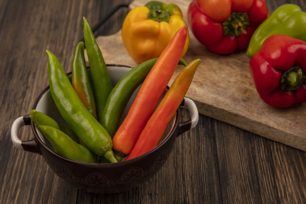 有机顶视图新鲜的绿色和橙色的辣椒在一个碗与黄色 红色和绿色的甜椒在一个木制的厨房板在木制表面营养一餐配料