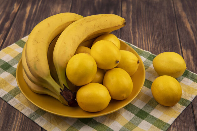 食物黄色盘子上圆形柠檬的顶视图 格子布上有香蕉 木头表面健康新鲜厨房