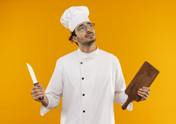 男看着身边想着的年轻男厨师穿着厨师制服 戴着眼镜 手里拿着砧板和刀厨师眼镜思考