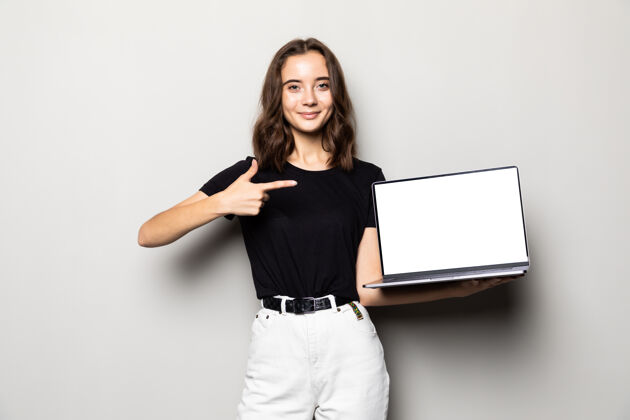 女人在灰色的空白笔记本电脑屏幕上 一个微笑的女人指着手指的肖像广告演示科技