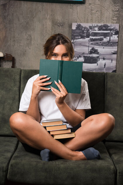 放松年轻女子躲在沙发上的书后面公寓女人积极