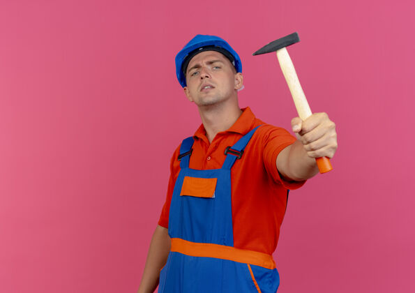 年轻自信的年轻男性建筑工人穿着制服 戴着安全帽 手持铁锤建筑工人穿锤子