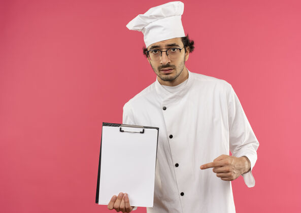制服悲伤的年轻男厨师穿着厨师制服 戴着眼镜 指着剪贴簿男穿年轻