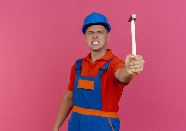 男性愤怒的年轻男性建筑工人穿着制服 戴着安全帽 手持铁锤工人佩戴粉色