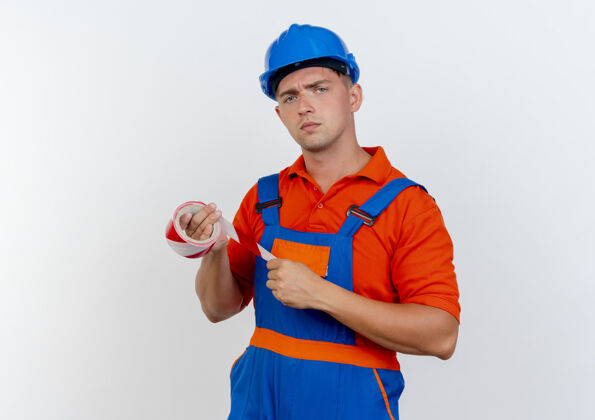 信心自信的年轻男性建筑工人穿着制服和安全帽拿着胶带头盔管道持有