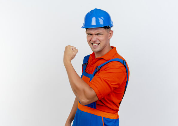 强壮自信的年轻男性建设者穿着制服 戴着安全帽做着坚强的手势建筑工人制服工人