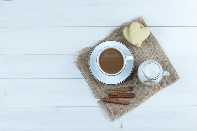 酒店顶视图咖啡杯饼干 肉桂棒 牛奶在木制和布袋的背景玻璃杯果酱早餐