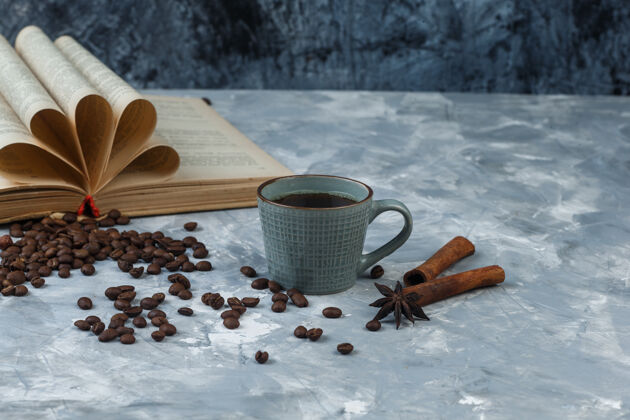 味道咖啡豆在一个木碗里与书 肉桂 咖啡杯特写上一个浅蓝和深蓝色大理石背景杯子食物讨论