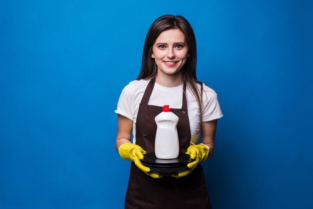 家庭主妇一个穿着围裙的年轻美女 盘子和洗碗皂一瓶装着空白标签的洗碗皂放在一堆干净的盘子上清洁女士洗涤剂