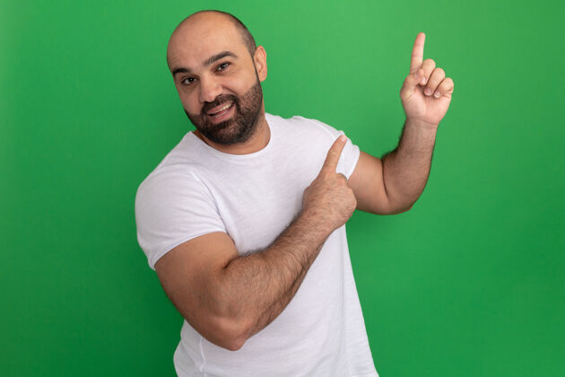 目录一个留着胡子的男人 穿着白色t恤 脸上带着微笑 食指指向一边 站在绿色的墙上 开心地微笑着站壁板欢呼