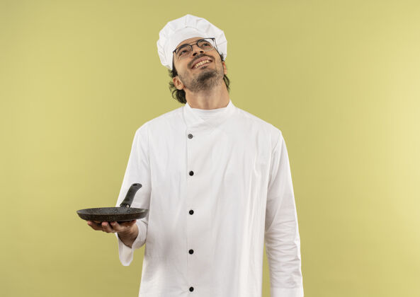 男人看着面带微笑的年轻男厨师 穿着厨师制服 戴着眼镜 手里拿着煎锅向上制服持有