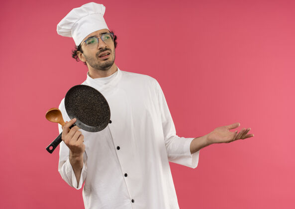 粉红色看着一旁未出炉的年轻男厨师穿着厨师制服 戴着眼镜拿着煎锅用勺子摊开手平底锅穿眼镜