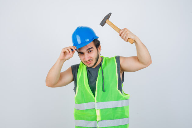 制服年轻的建筑工人穿着工作服 手持头盔和锤子 看上去很自信 正对着前方表情人自信