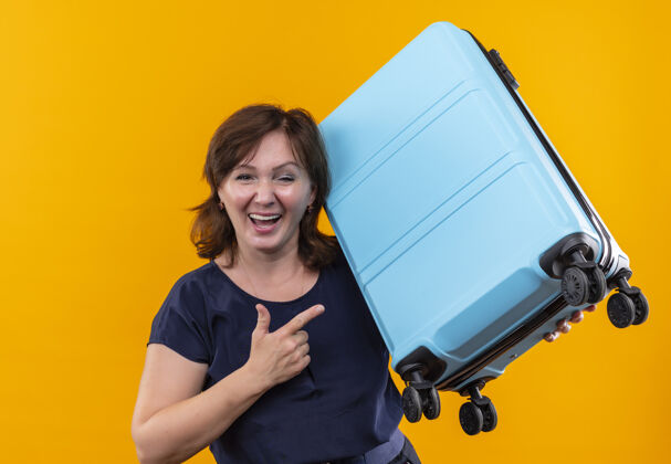 手提箱笑容可掬的中年旅女抱着并指着手提箱上旅行点老年人
