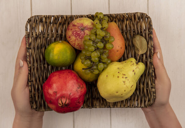 水果俯视图：白墙上的篮子里 一个女人手里拿着苹果 石榴 橘子和葡萄顶部石榴葡萄