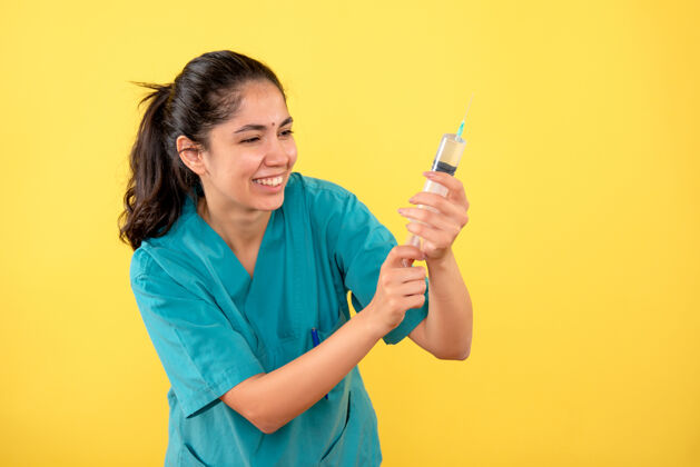 成人正面图黄色背景上带注射器的快乐年轻女医生年轻女医生肖像微笑