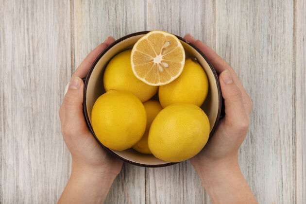 美味女性手拿着一碗健康的柠檬在灰色木头表面的俯视图柠檬配料碗