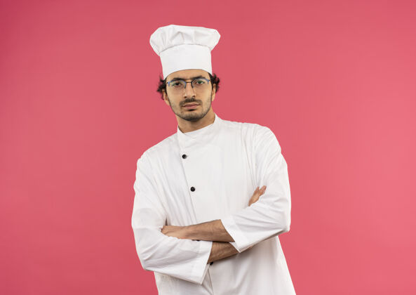 烹饪自信的年轻男厨师穿着厨师制服和眼镜双手交叉粉色厨师制服