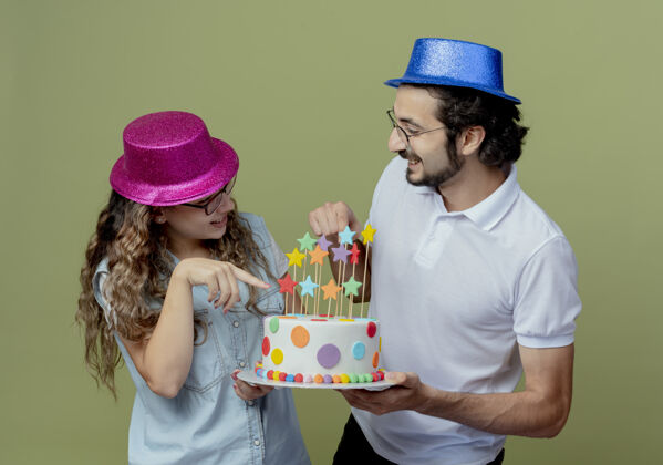 橄榄色一对戴着粉色和蓝色帽子的年轻夫妇高兴地看着对方 指着手里的生日蛋糕蛋糕绿色手