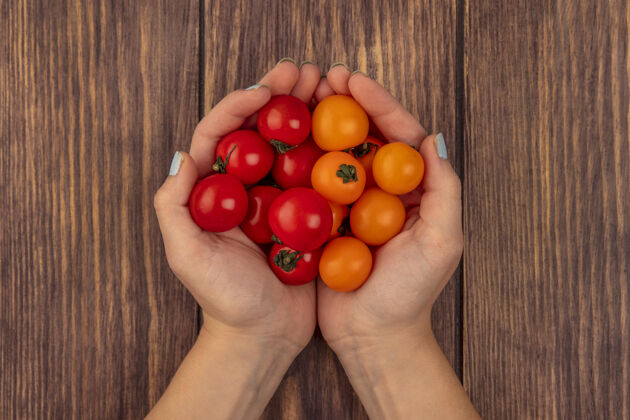 美味顶视图中的女性手拿着新鲜的樱桃红色和橙色的西红柿在木制表面有机农业配料