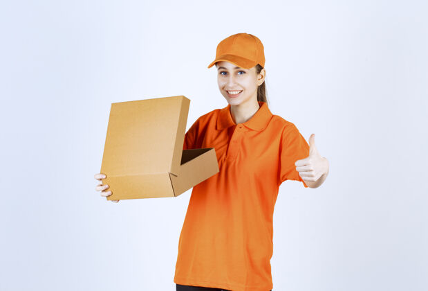 姿势身着橙色制服的女快递员手持一个打开的纸板箱 并显示正面手势年轻成人订单