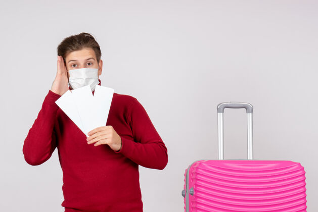 快乐戴着面具的年轻男子在白墙上拿着飞机票的正视图假期年轻男性前面