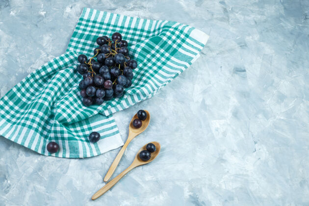 木材黑葡萄放在木汤匙里 背景是灰色的厨房毛巾平铺秋天水果勺子