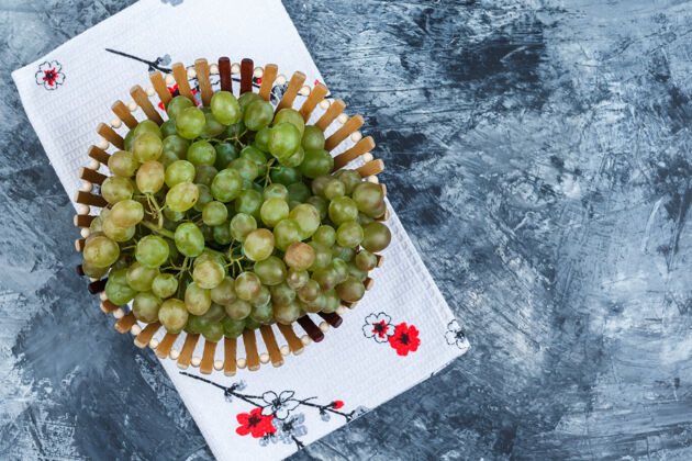 多汁绿色的葡萄在一个篮子里平放在肮脏的石膏和厨房毛巾的背景季节酒厂葡萄藤