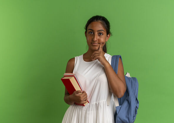 女生年轻的女学生背着书包拿着笔记本把手指放在脸颊上绿色戴着脸颊