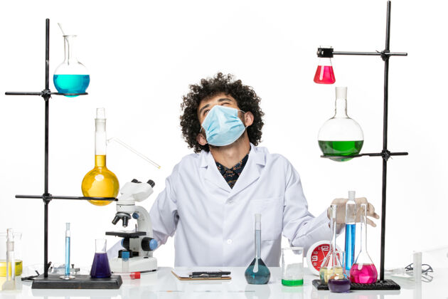 科学前视图男性化学家穿着医疗服 戴着面罩 坐在浅白的空间里 拿着溶液病毒实验室实验室外套