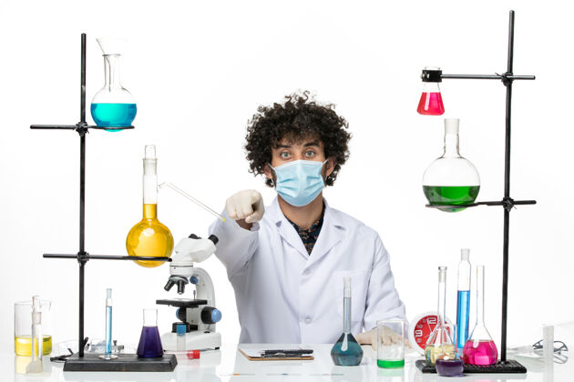 医生正面图：男药剂师穿着医疗服 戴着口罩 坐在一个空白处 上面有不同的溶液化学只是实验室外套
