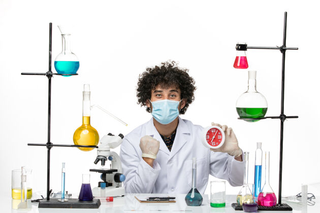 科学正面图：男药剂师穿着医疗服 戴着面罩 白色桌子上拿着红色的钟面罩手持办公桌