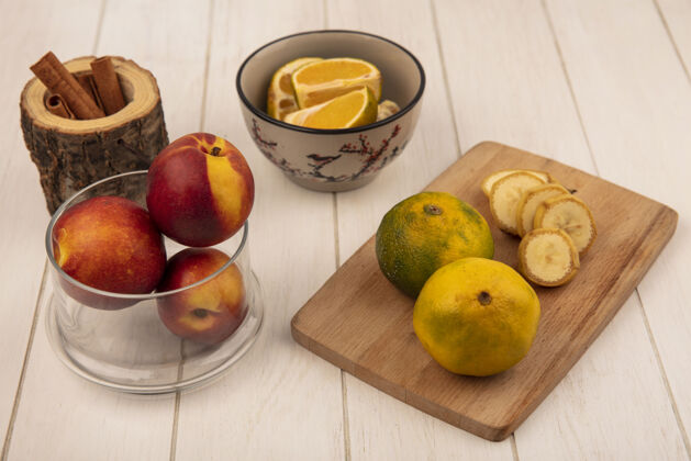成熟在白色木质表面的玻璃碗上放着香蕉片和桃子的木制厨房板上的新鲜橘子俯视图板厨房柑橘