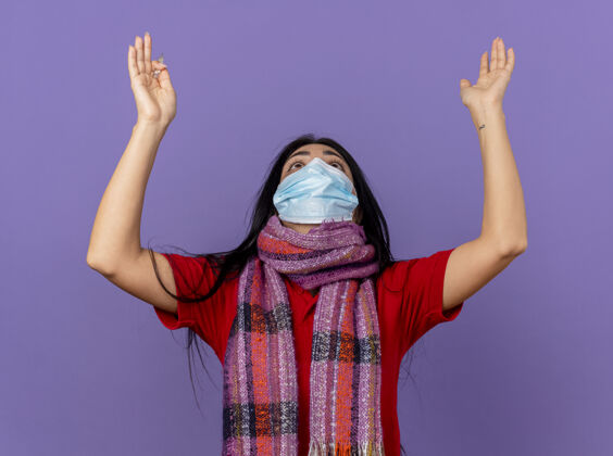 养育年轻的白种人患病的女孩戴着口罩和围巾拿着温度计抬头举手祈祷和祝福上帝隔离在紫色的墙上祈祷体温计疾病
