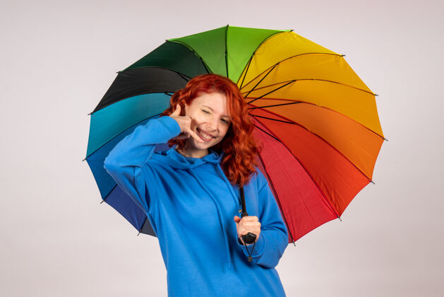 伞白色墙壁上带着彩色雨伞的年轻女性的正视图保护掩护雨天气