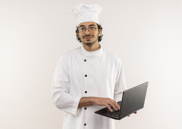 眼镜面带微笑的年轻男厨师穿着厨师制服 戴着眼镜 拿着笔记本电脑隔离在白色的墙上男性厨师年轻