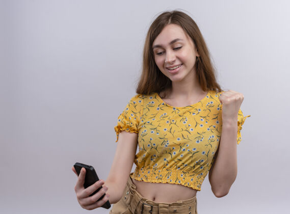 女人孤零零的白墙上 一个微笑的年轻女孩举着手机 举起拳头电话女孩手机