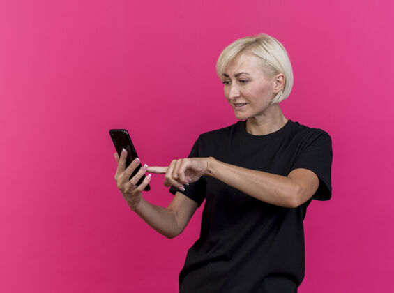 手机高兴的中年金发斯拉夫女子拿着手机看着用它隔离在深红色墙上的复制空间电话女人金发