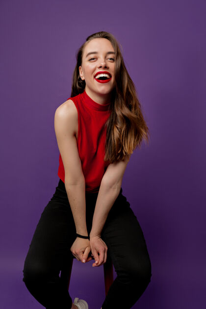 享受性感可爱的女孩 带着美妙的微笑 穿着红色上衣 在紫罗兰色上大笑椅子卷发红色
